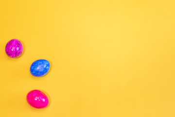 Three colored Easter eggs on a yellow background. Top view. Happy Easter card  with free, empty space. Minimal Easter concept.