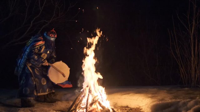 The shaman performs a dance with a tambourine around the fire.