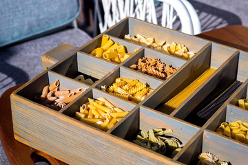 wooden box with cells for an assortment of different types of pasta in a bakery market, closeup.