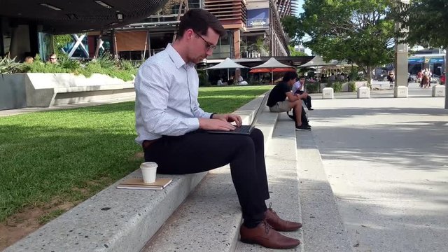 Businessman sitting in park sending emails off laptop.