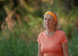 A middle-aged woman in spostswear takes a breather in a park  after jogging