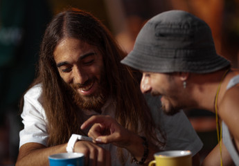 Two young man sitting at a table, smiling while viewing the smart watch of one of them