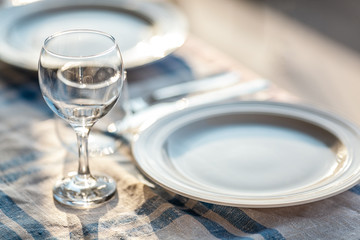 A fragment of a laid table with a tablecloth, a couple of plates, glasses and cutlery