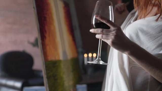 Girl painting while holding a glass of wine