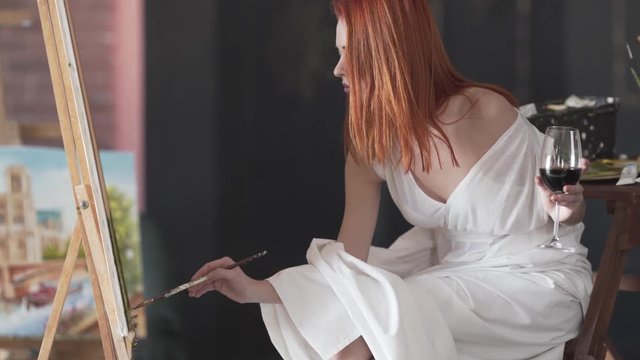 Beautiful redheaded girl painting while drinking wine