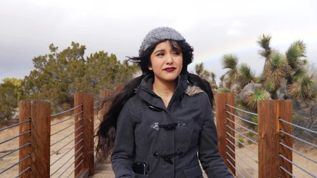 Attractive young woman in a freezing cold and windy storm with a colorful rainbow in the cloudy sky SLOW MOTION.