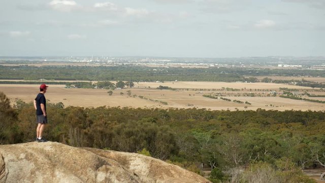 Man looking out from the You Yangs National Park, Victoria Australia. Man gets smart phone out and takes a picture of the views. LOCKED DOWNS SHOT.