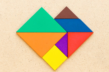 Color tangram puzzle in heart shape on wood background