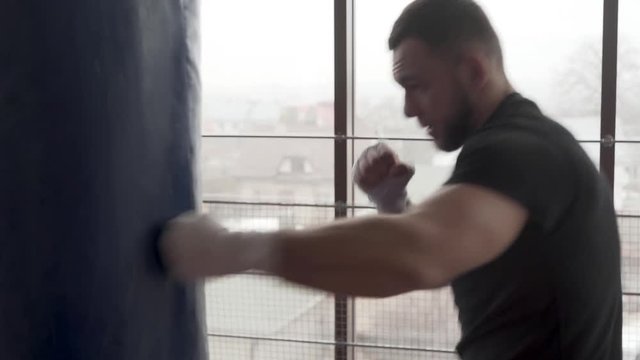 Young athletic man in a boxing gloves is training boxing in a gym. He is working on his boxing techniques with a punching bag.