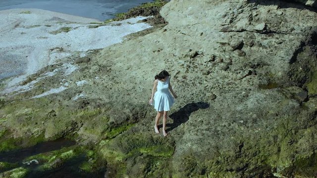 Aerial slow motion shot of pretty girl in white dress walk on the beach