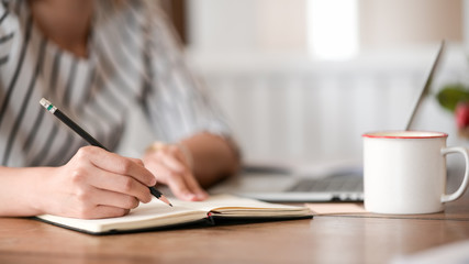 Closes up woman hand is writing on notepad with pen in office.