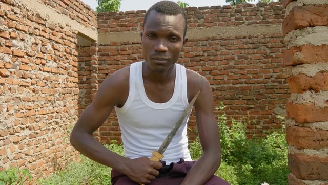 A young African gangster is holding a knife in an abandoned building in rural Africa.