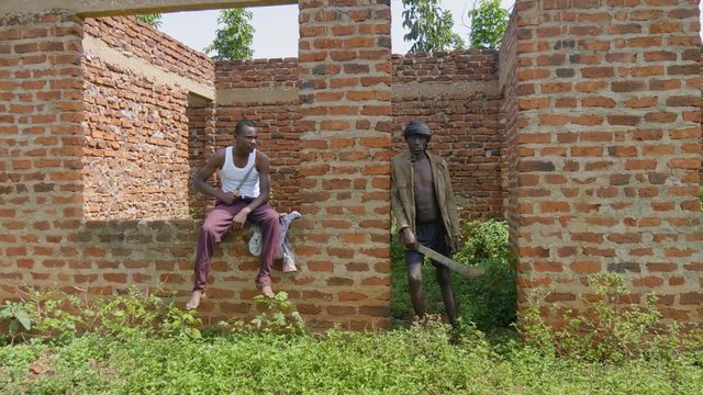 Two young African gangsters with weapons looking tough in a unfinished building in rural Africa.