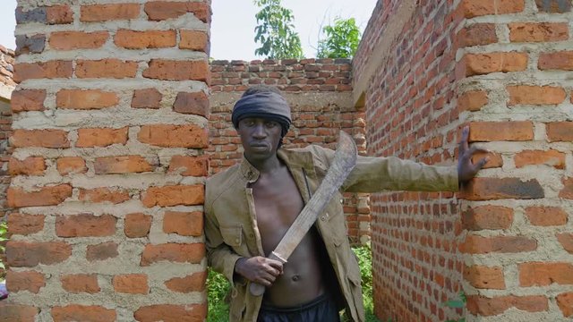 A shot of a young African gangster holding a machete in an abandoned house in rural Africa.