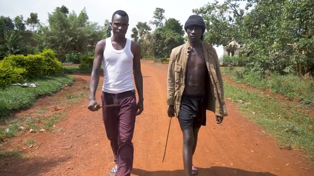 A front facing slow motion moving shot of two African gangsters with weapons walking in rural Africa.