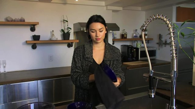 A young woman finishes doing the dishes in a nice kitchen.