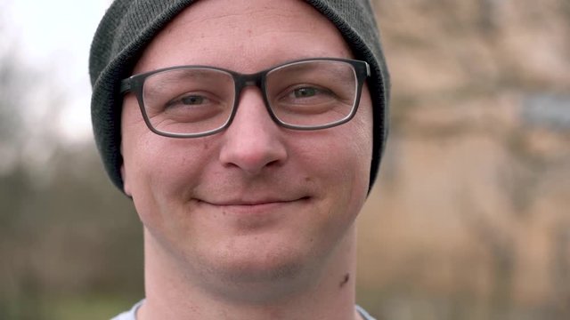 Young man wearing glasses and a hat looks into the camera and laughs