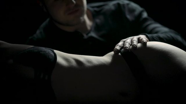 A man gently runs his hands over a woman's body in the dark