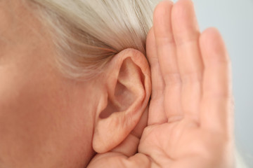 Mature woman with hearing problem on light background, closeup