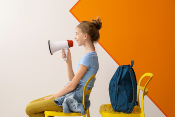 Portrait of cute teenage girl with megaphone sitting on chair against color background