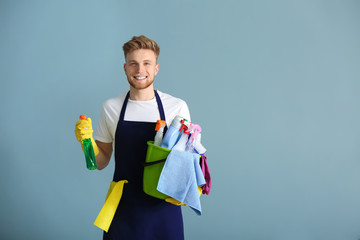 Portrait of male janitor with cleaning supplies on grey background