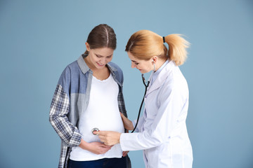 Gynecologist examining young pregnant woman on grey background