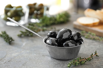 Ladle with tasty olives on grey table