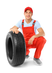 Young male mechanic in uniform with car tire on white background