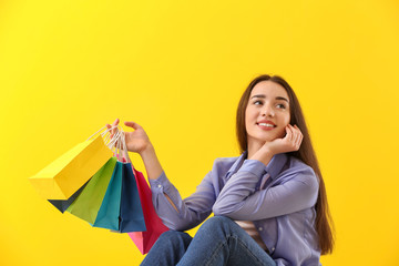 Fototapeta na wymiar Happy young woman with shopping bags on color background