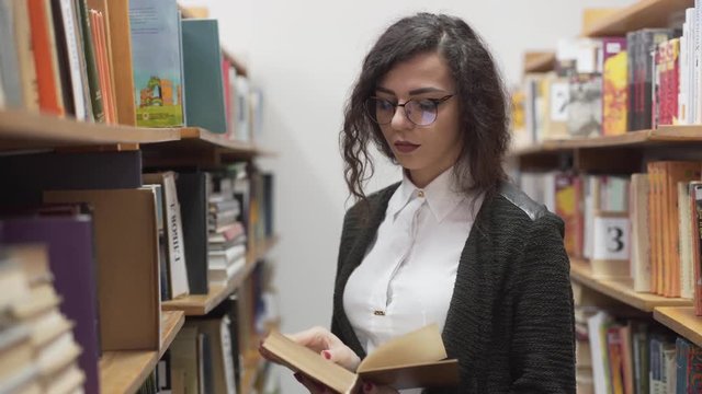 Beautiful librarian reads a book in the stacks of a library.