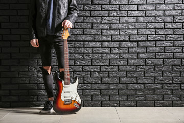 Handsome young man with guitar near dark brick wall