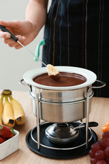 Woman dipping fresh banana into chocolate fondue at table