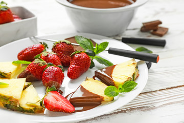 Plate with fresh pineapple, strawberry and melted chocolate on white table