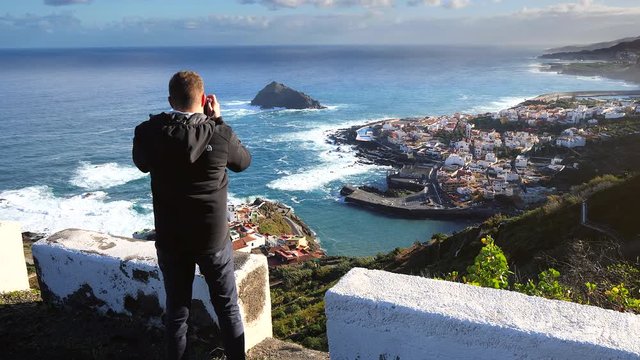 View of a tourist taking a photo of the view from the cliff of Garachico in the island of Tenerife (Canary Islands)