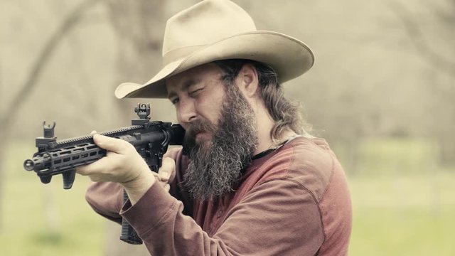 Vintage look, front angle of a cowboy carefully aiming and shooting rounds of ammo from a rifle with powerful recoil, slow motion 23.98 fps.