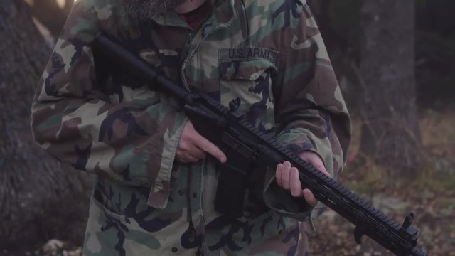 Medium shot of a man wearing camouflage, holding a weapon & listening for wildlife in the woods, 60 fps.