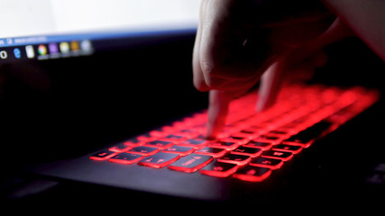 Typing with two fingers on a laptop with red keyboard in the darkness. Close up clip. Artificial...