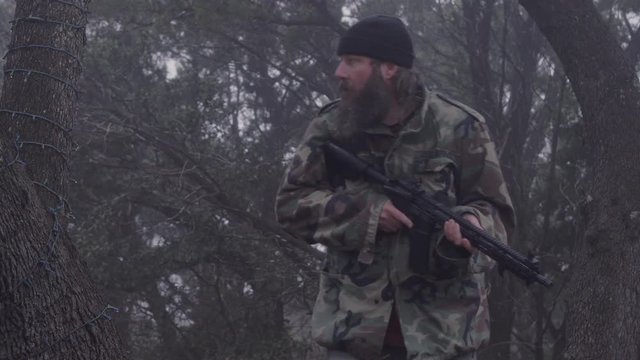 A camouflaged hunter quietly moves in the cold misty forest, armed with a weapon, listening for wild animals, 23.98 fps.