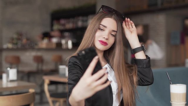 Beautiful young woman in a blazer poses for some selfies in a coffeshop.