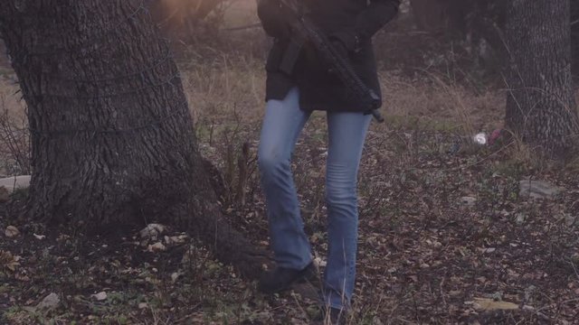 A female hunter holding a weapon, treads carefully and quietly in the forest looking for wild animals, slow motion 29.97 fps.