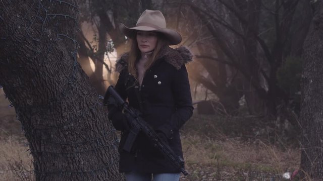 A female hunter holding a weapon, looking around in the cold forest for movement, slow motion 29.97 fps.