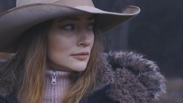 Vintage look, close up of a woman wearing a cowboy hat standing in the woods, rugged up for winter, 60 fps.