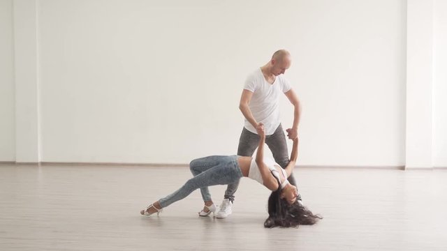 Wide shot of a couple dancing. The man spins the woman, drops her, then catches and suspends her inches from the ground.