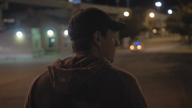 View From Behind Of A Man Walking Down A City Street At Night