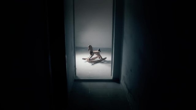 A scary rocking horse, abandoned in a room with a flickering light. Nobody in sight. Long shot.