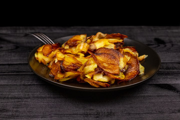 Fried homemade potato chips in a black plate on a wooden rustic background