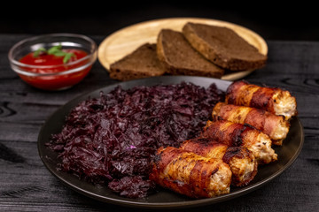 Fried homemade grilled sausages or chevapchichi with stewed sauerkraut, and slices of rye bread and tomato sauce on a wooden rustic background