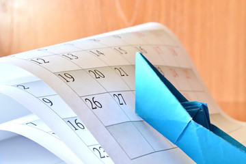 Origami blue paper boat rises to top on the sheets of monthly calendar folded like high stormy...