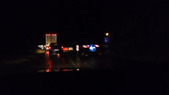 Traffic jam and semi trucks driving on rural road with road works and signt in the dark night during rein weather