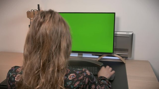 Woman working in a modern personal computer, with Mock-up Green Screen Display Standing on the Desk of the Office.